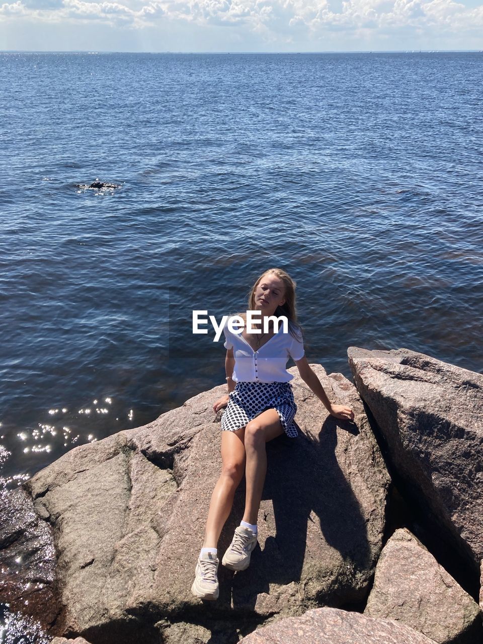 rear view of woman sitting on rock by sea