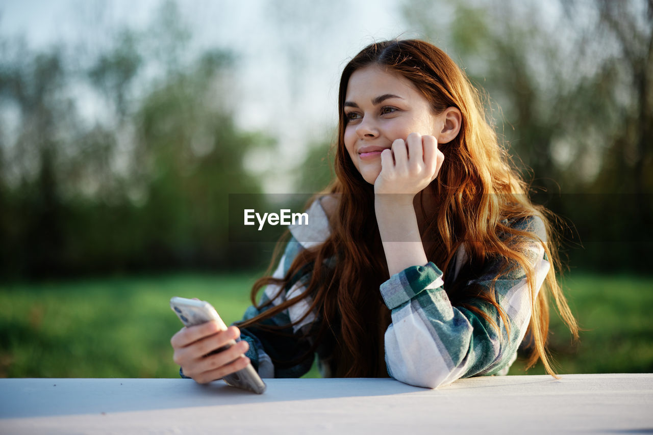 young woman using mobile phone while sitting at park