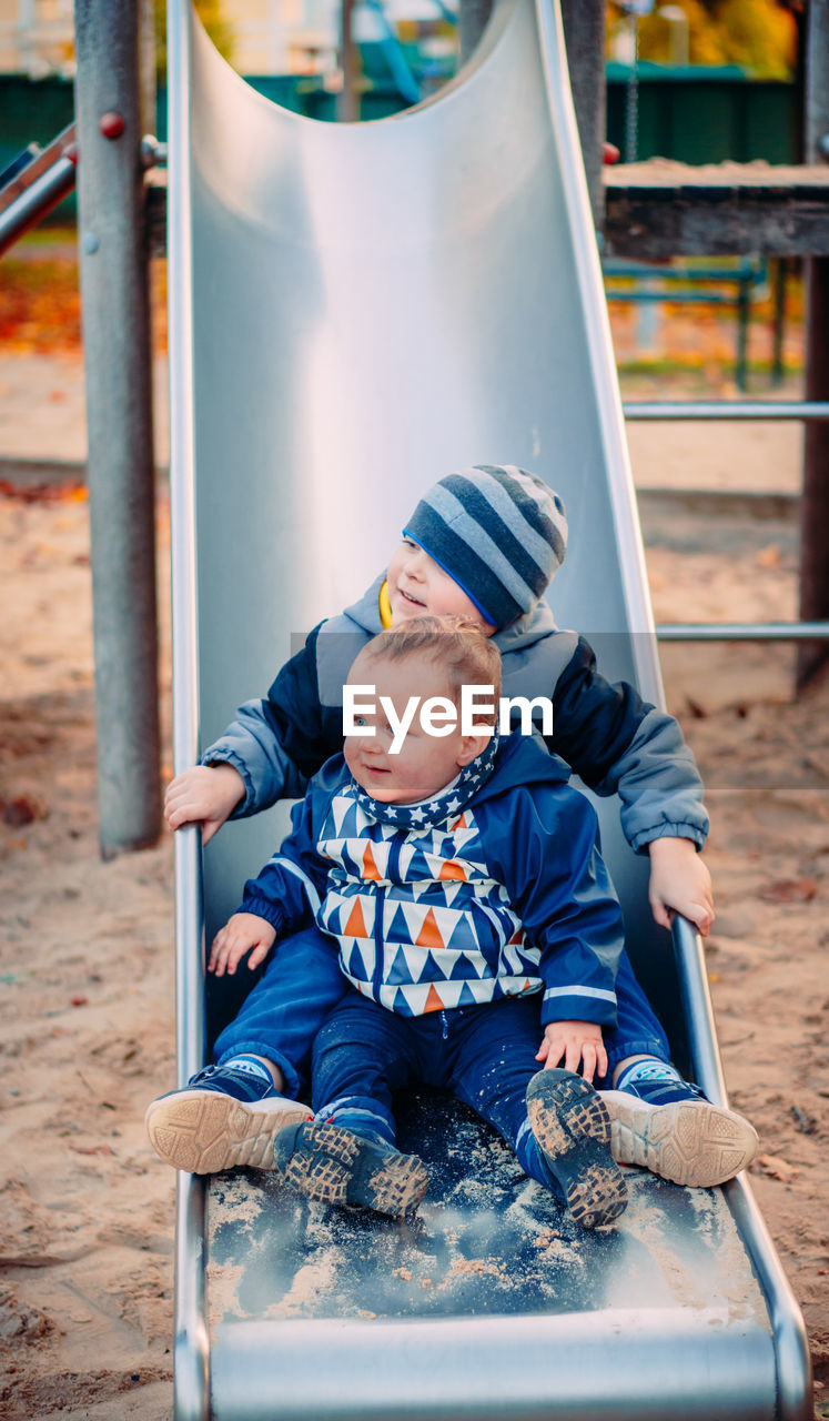 Cute sibling sitting on slide at playground