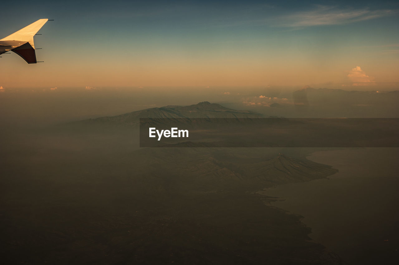 AERIAL VIEW OF MOUNTAINS AGAINST SKY AT SUNSET