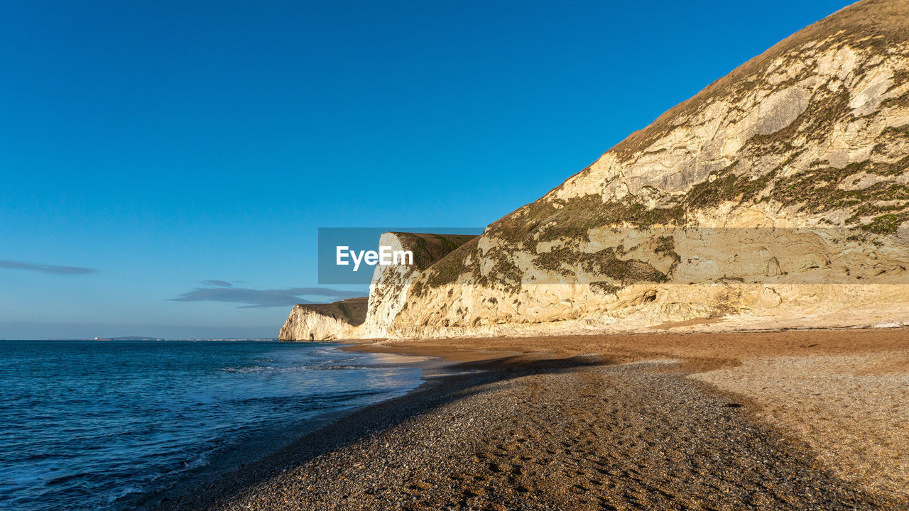 Rock formations on beach against clear blue sky