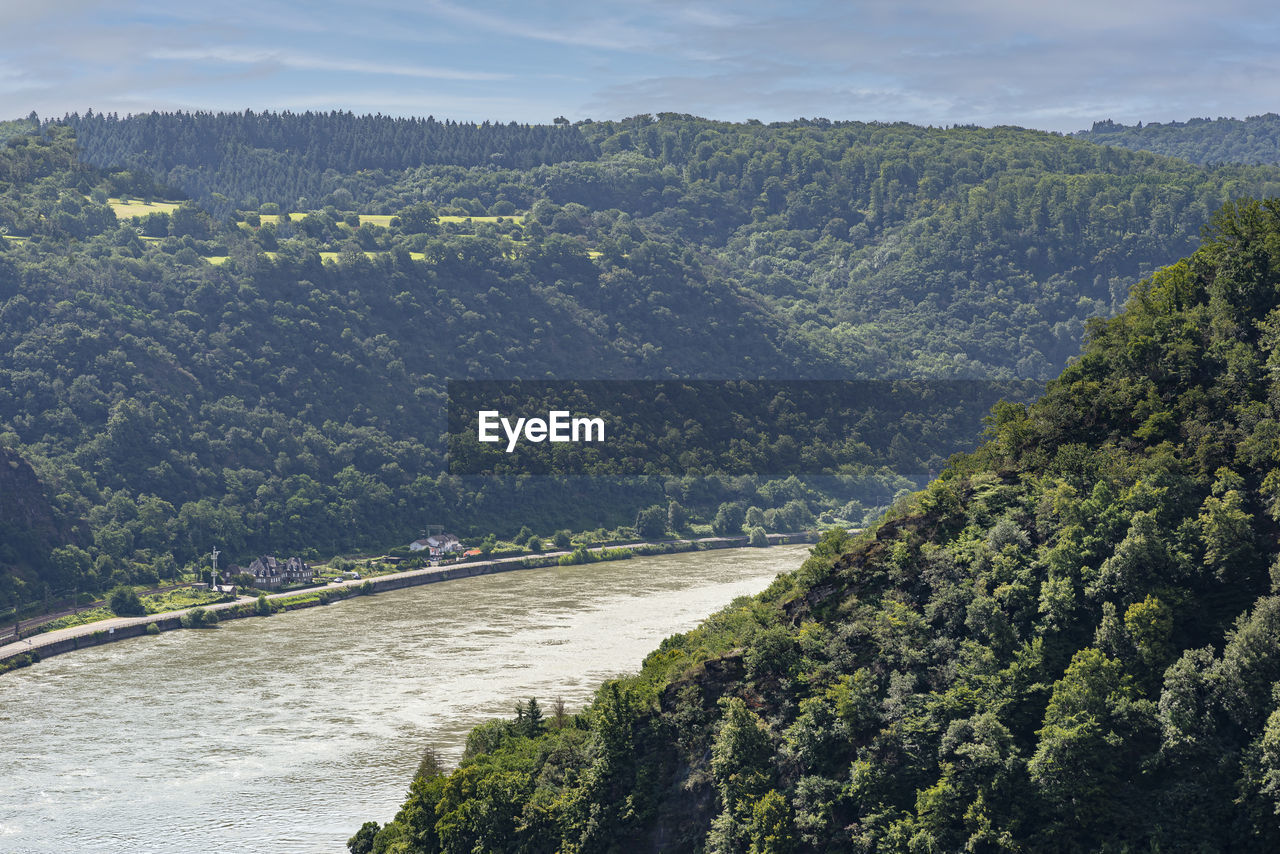 The river rhine in western germany flows between the hills covered with forest, buildings visible.