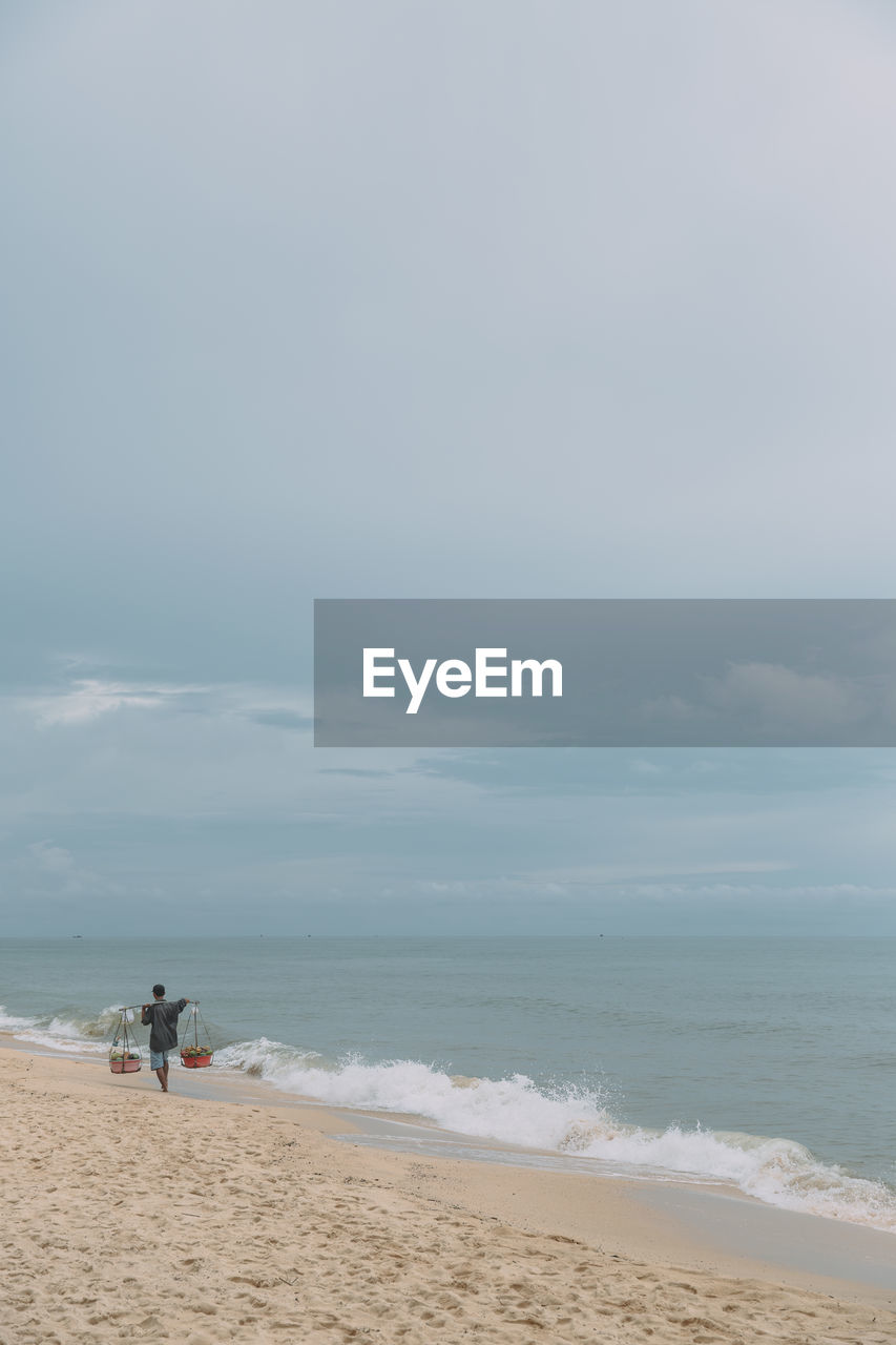 Rear view of man walking on beach against sky