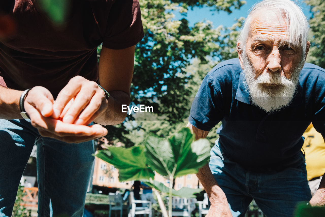 Retired senior man standing by male volunteer at back yard