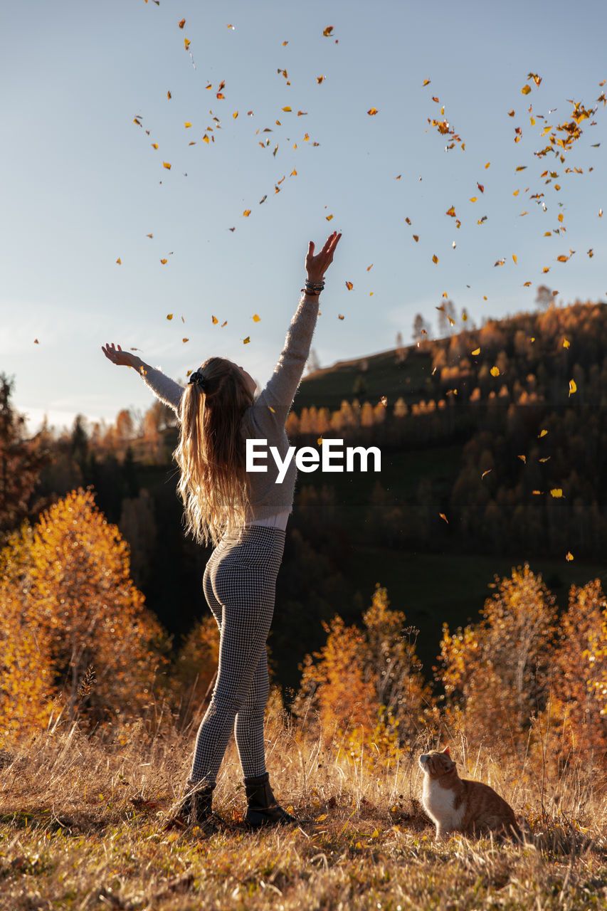 WOMAN STANDING BY TREE AGAINST SKY IN BACKGROUND