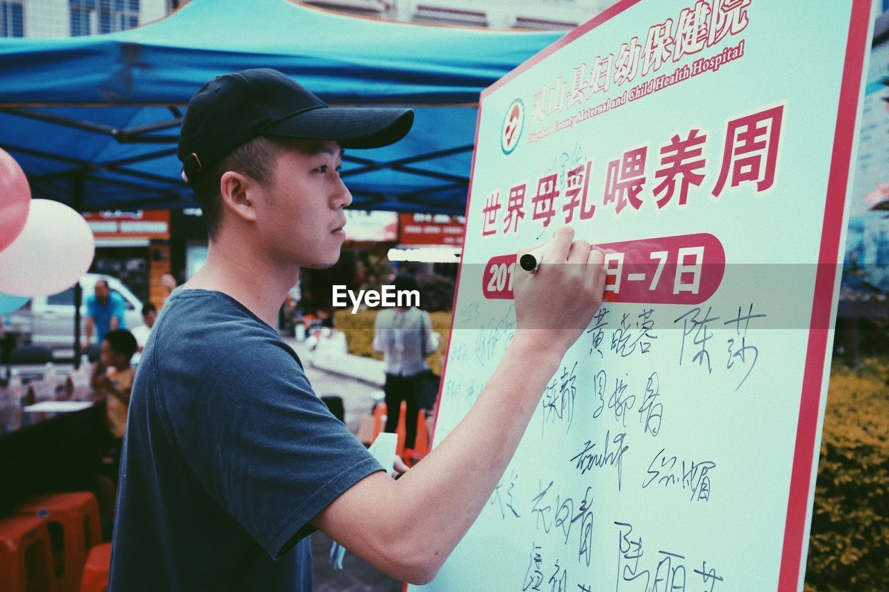 SIDE VIEW OF YOUNG MAN STANDING BY TEXT ON WALL