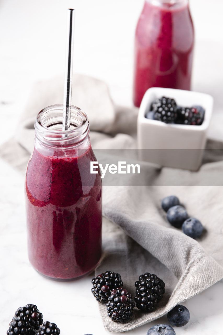 Fresh smoothie made from berries on glass bottles and a reusable metal straw to drink it.