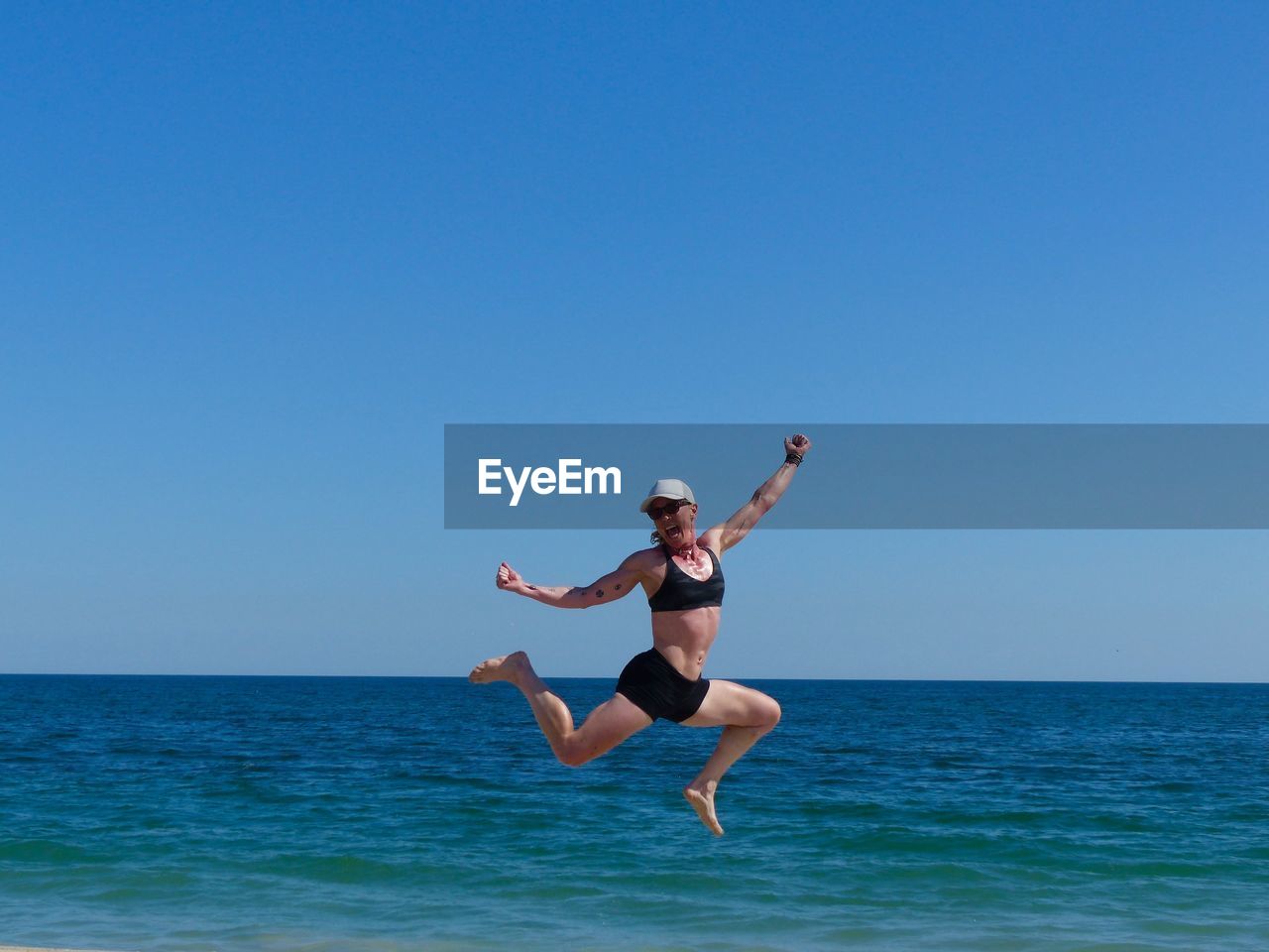 Happy athlete in mid-air at shore against clear sky