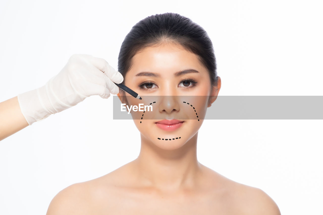 Cropped hand marking on women face against white background