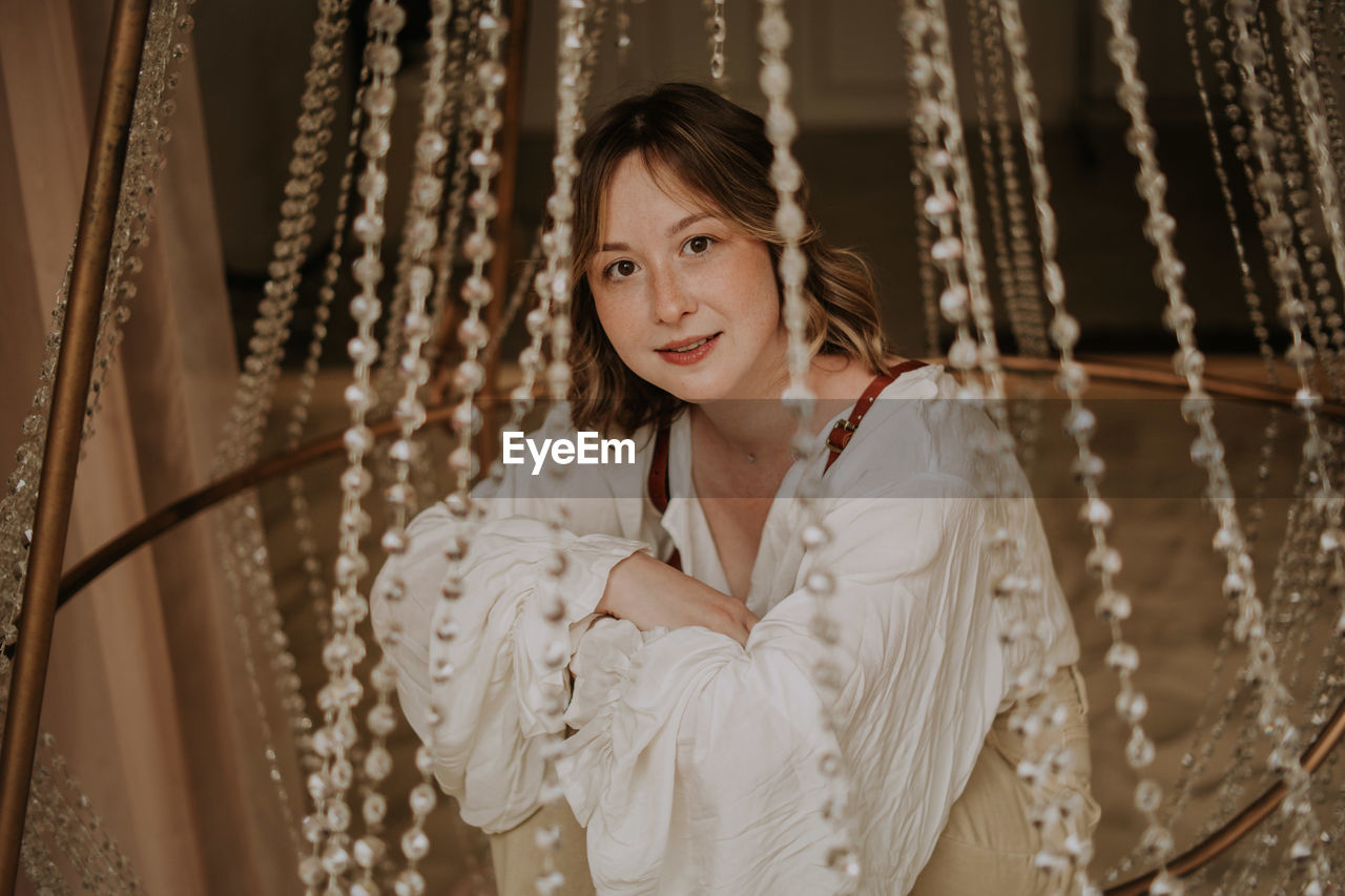 Young female in victorian shirt sitting in giant crystal chandelier and smile