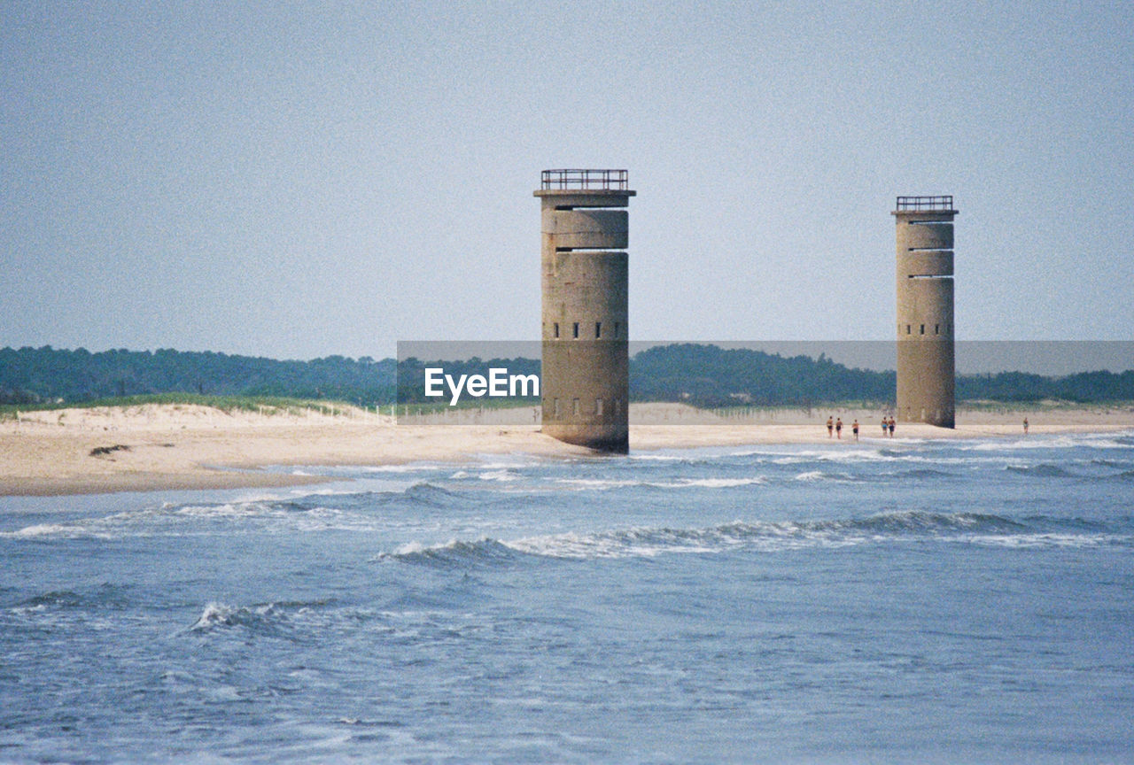 water, sea, tower, ocean, coast, sky, beach, lighthouse, land, architecture, nature, built structure, no people, shore, day, clear sky, wave, outdoors, scenics - nature, building exterior, wind wave, environment, blue, breakwater, guidance, travel destinations, travel