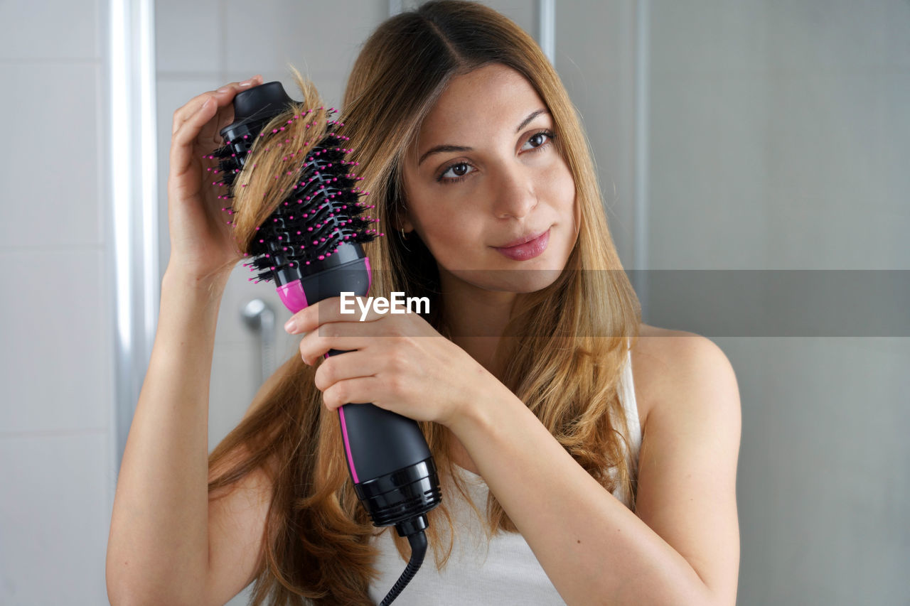 Girl using brush hair dryer to style hair at the mirror on bathroom