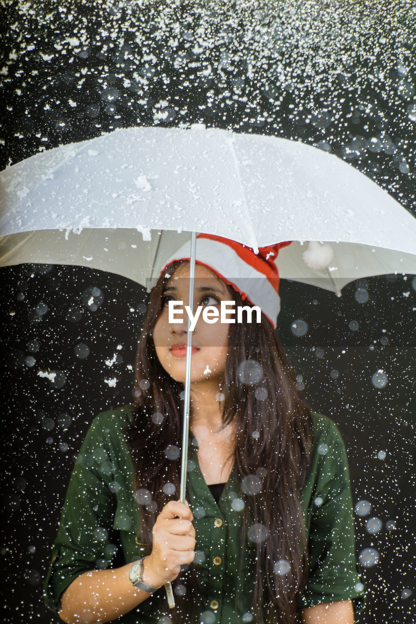 Young woman with umbrella during snowfall against black background