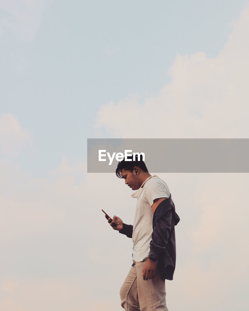 Side view of man using mobile phone against sky while music on