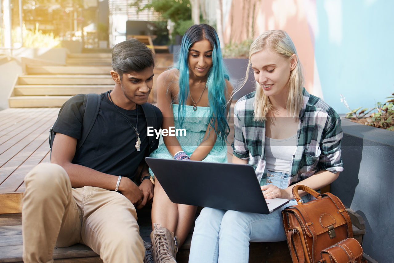 Friends using laptop while sitting outdoors