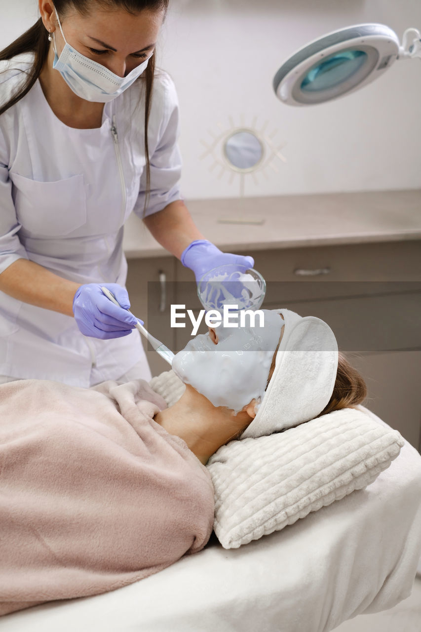 Cosmetologist apply skin mask with brush, care and treatment procedure in modern aesthetic clinic