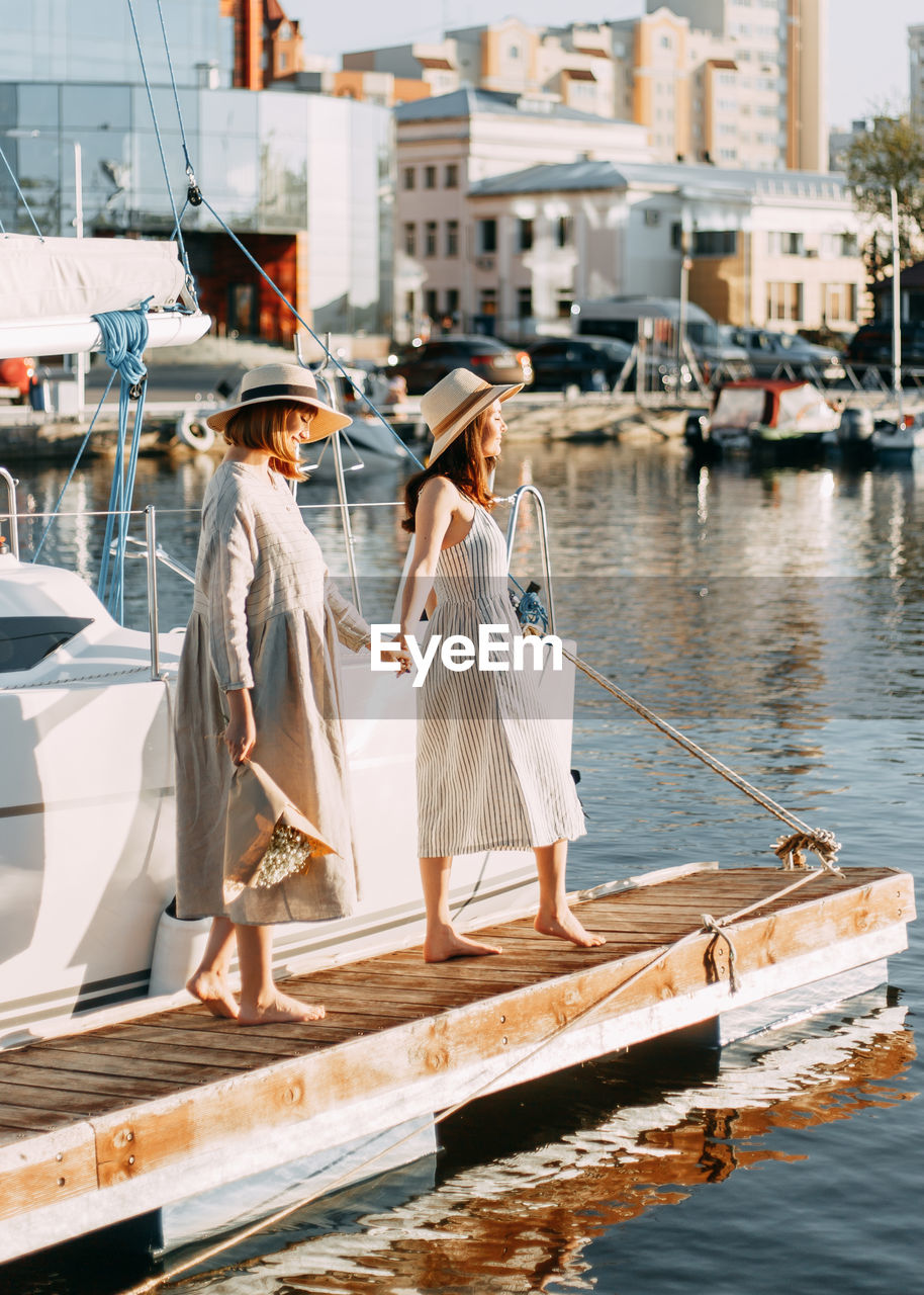 Two women friends walk along the pier along the boats and yachts in summer
