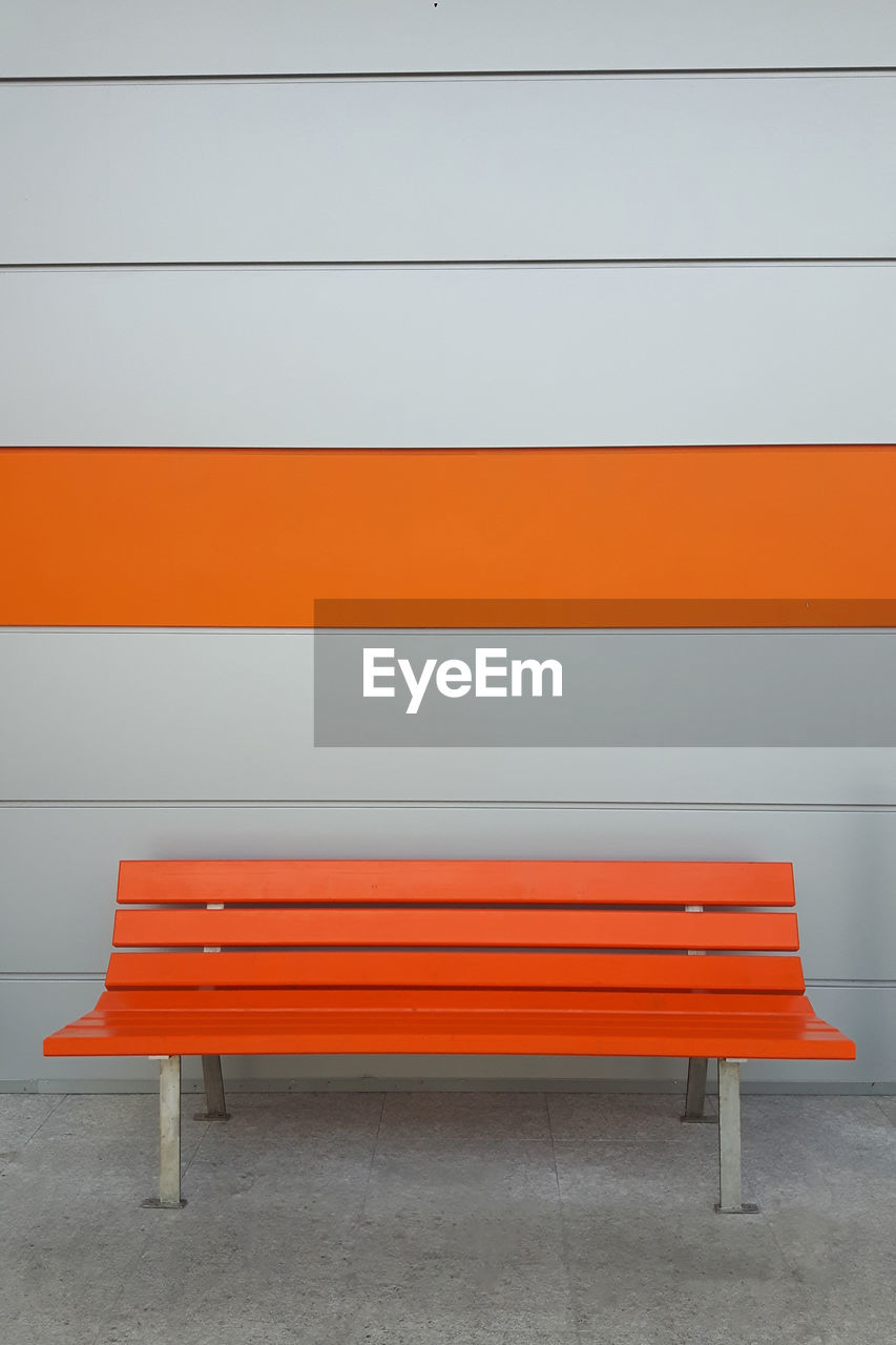 Empty orange bench by wall