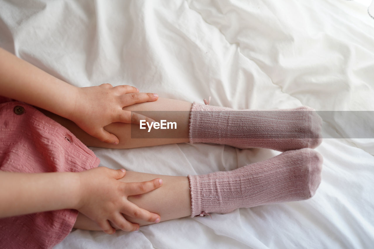 Child's girl legs in pink socks with hands on a bed in a cozy home