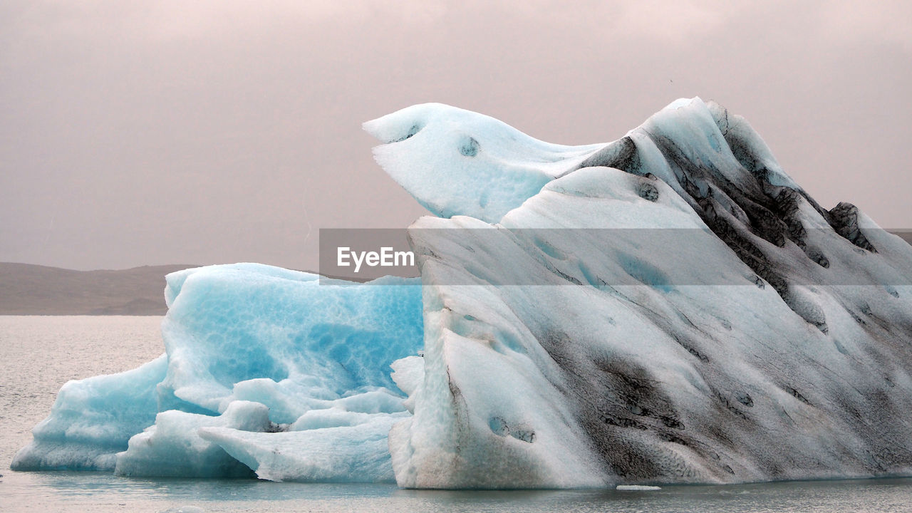 Iceberg on sea against sky at sunset