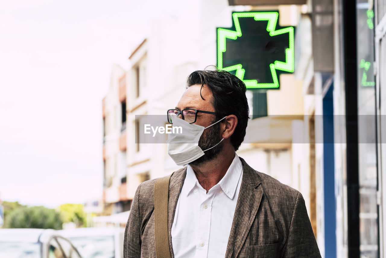 Mature man wearing face mask looking away against building