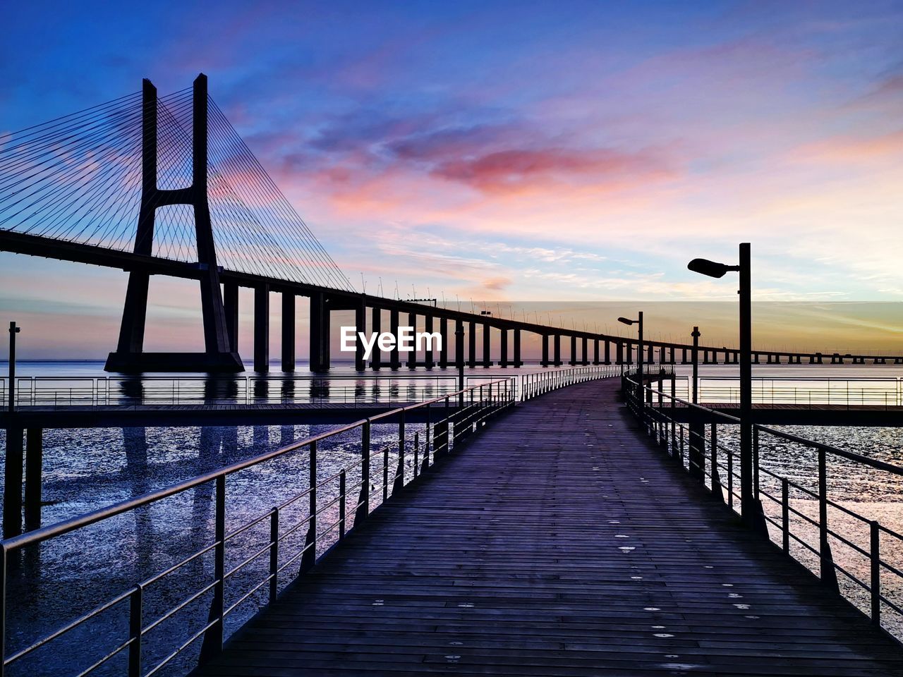 Pier over sea against sky during sunrise and vasco da gama bridge at tejo river