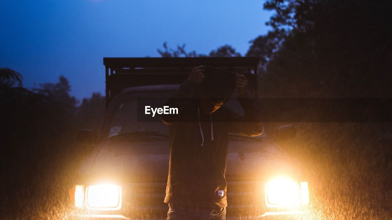 Man standing against illuminated headlight of car