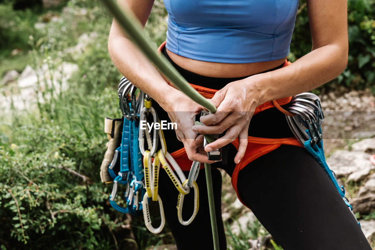 Midsection of female hiker tying rope on harness while preparing for rappelling
