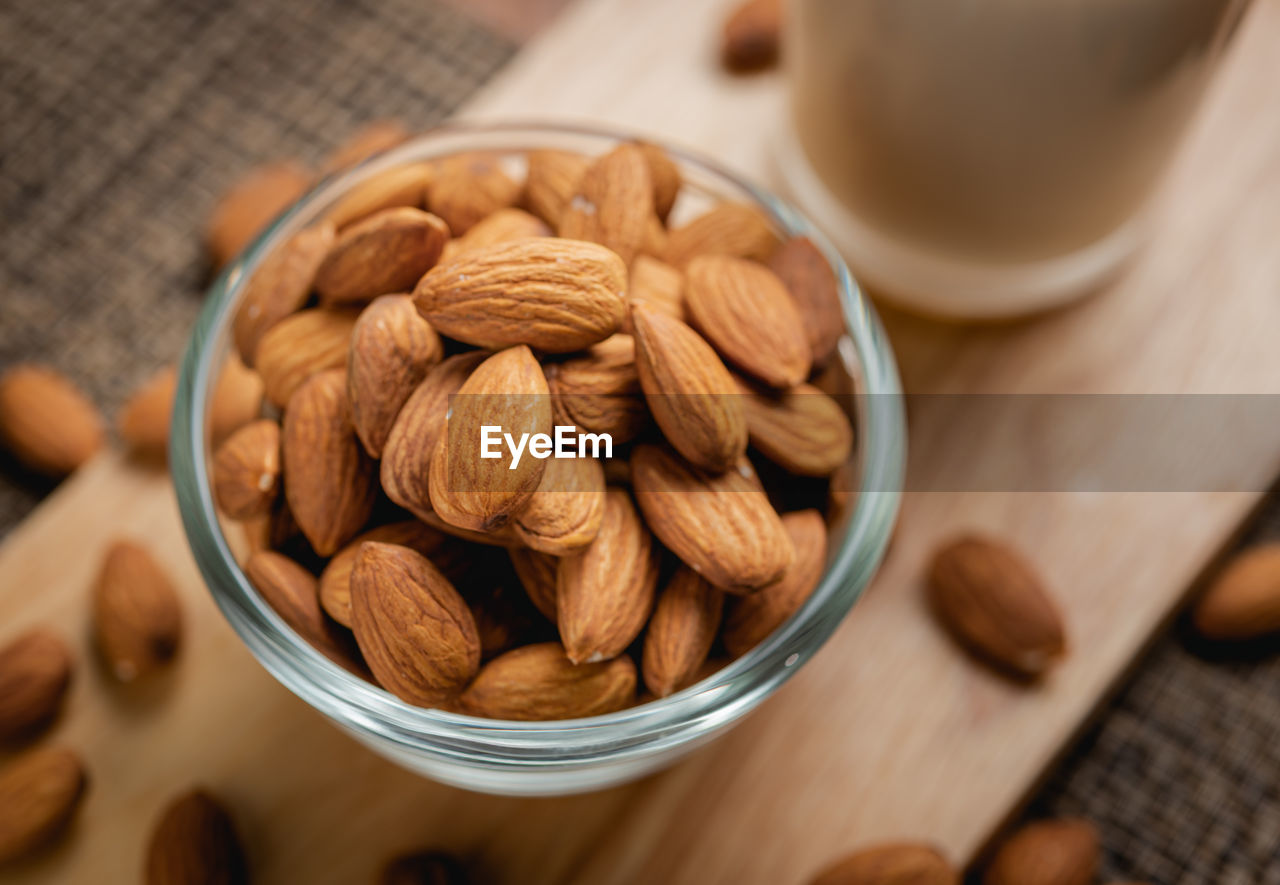 Almond milk in the glass with almond in the glass bowl on the wooden table.