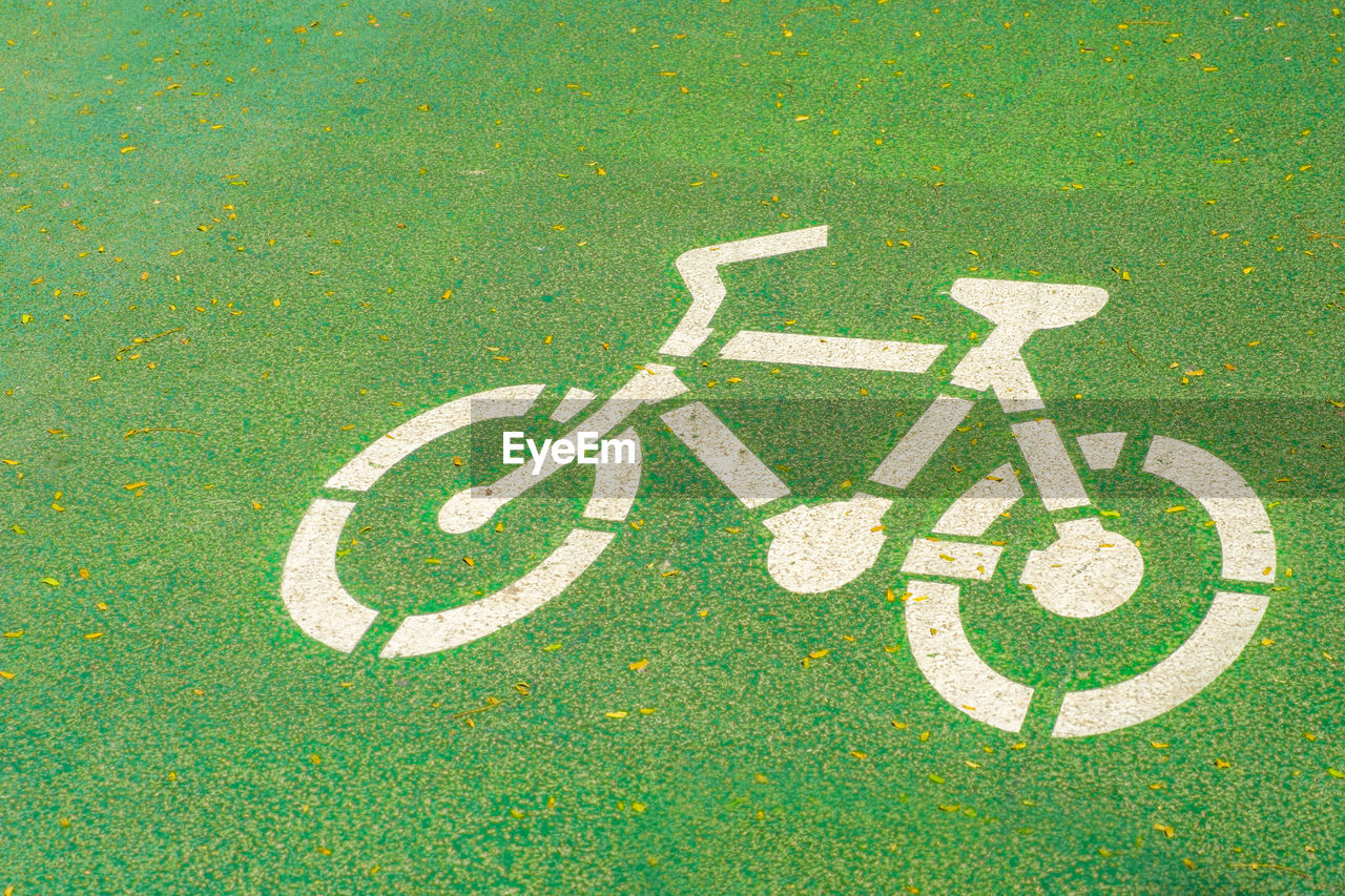 Old white bicycle road sign on green road floor for background.