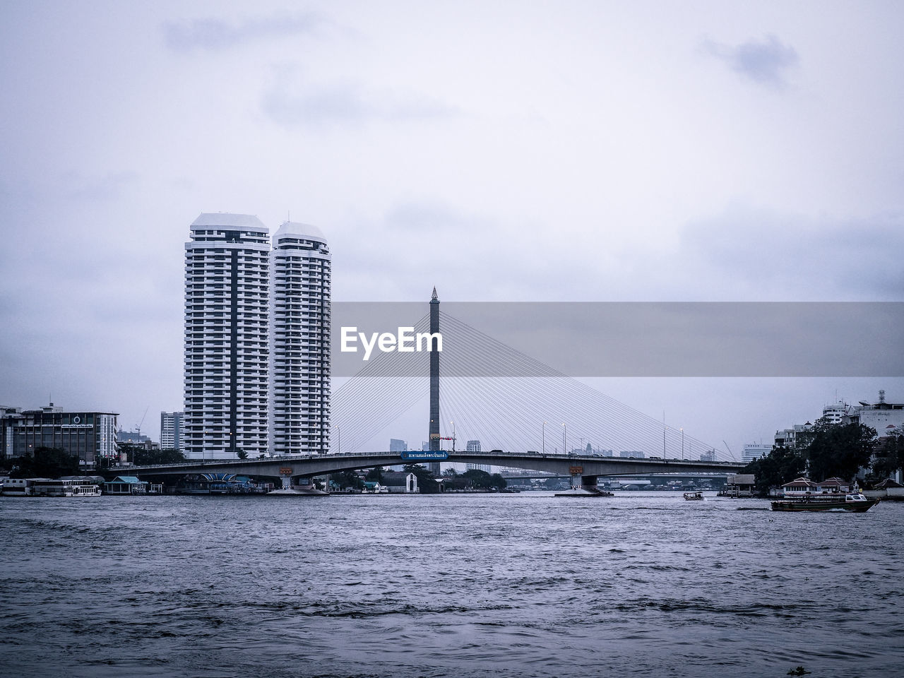 Bridge over river by city buildings against sky