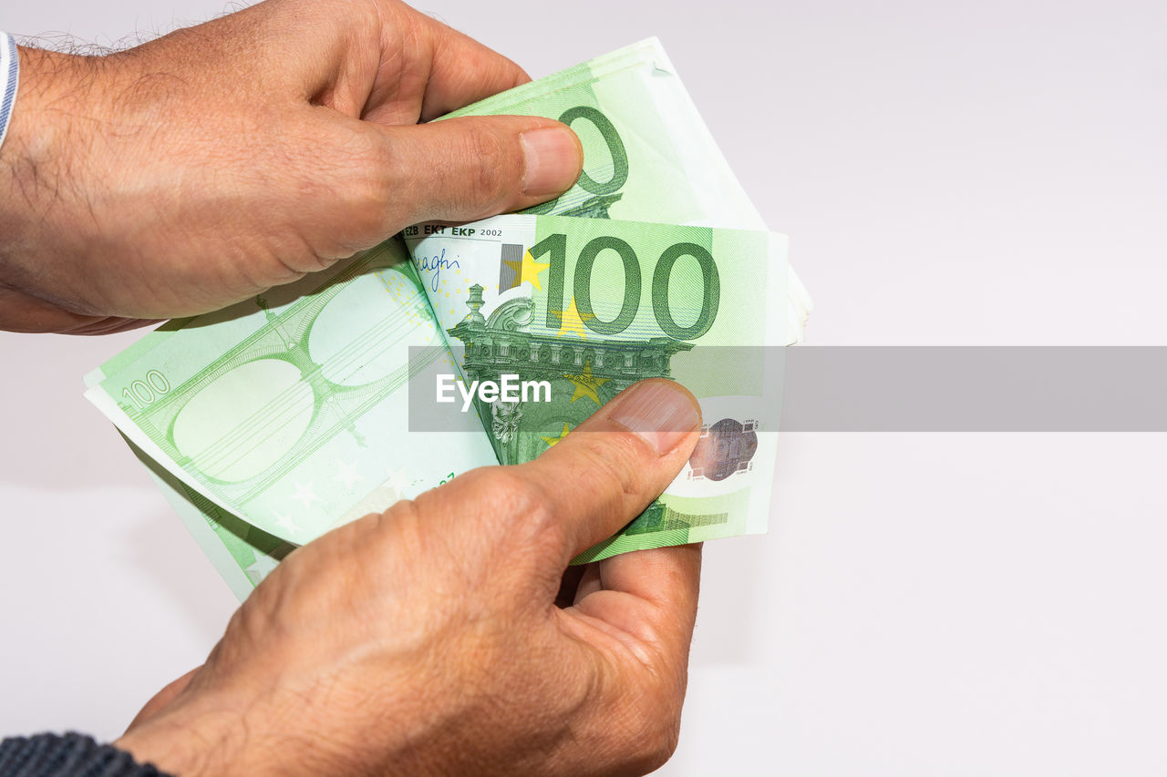 MIDSECTION OF MAN HOLDING HANDS OVER WHITE BACKGROUND