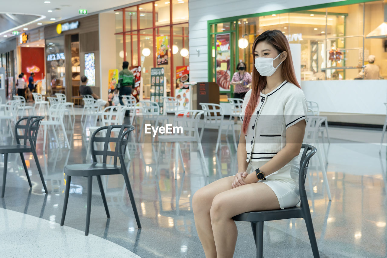 Beautiful woman wearing mask sitting on chair at shopping mall