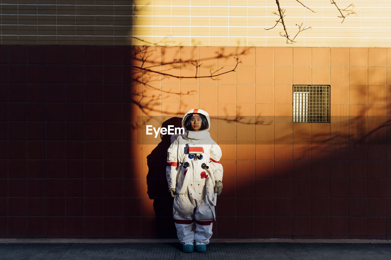 Woman astronaut in space suit standing by wall during sunset