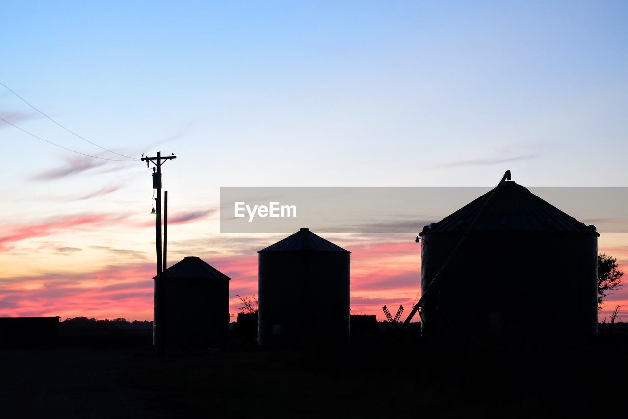 Silhouette silos on field against sky during sunset