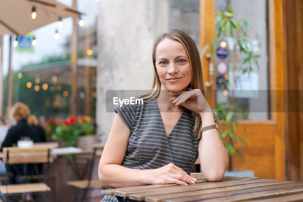 Confident young woman sitting in a street cafe at a table in a gray striped