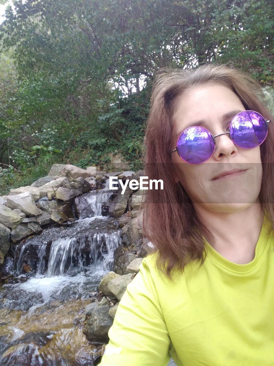 waterfall, one person, portrait, sunglasses, water, glasses, leisure activity, women, nature, front view, fashion, child, day, lifestyles, looking at camera, plant, childhood, rock, human face, headshot, female, smiling, outdoors, tree, hairstyle, casual clothing, beauty in nature, long hair, vacation, clothing, spring, person, young adult, standing, green, land, adult, goggles, forest, happiness