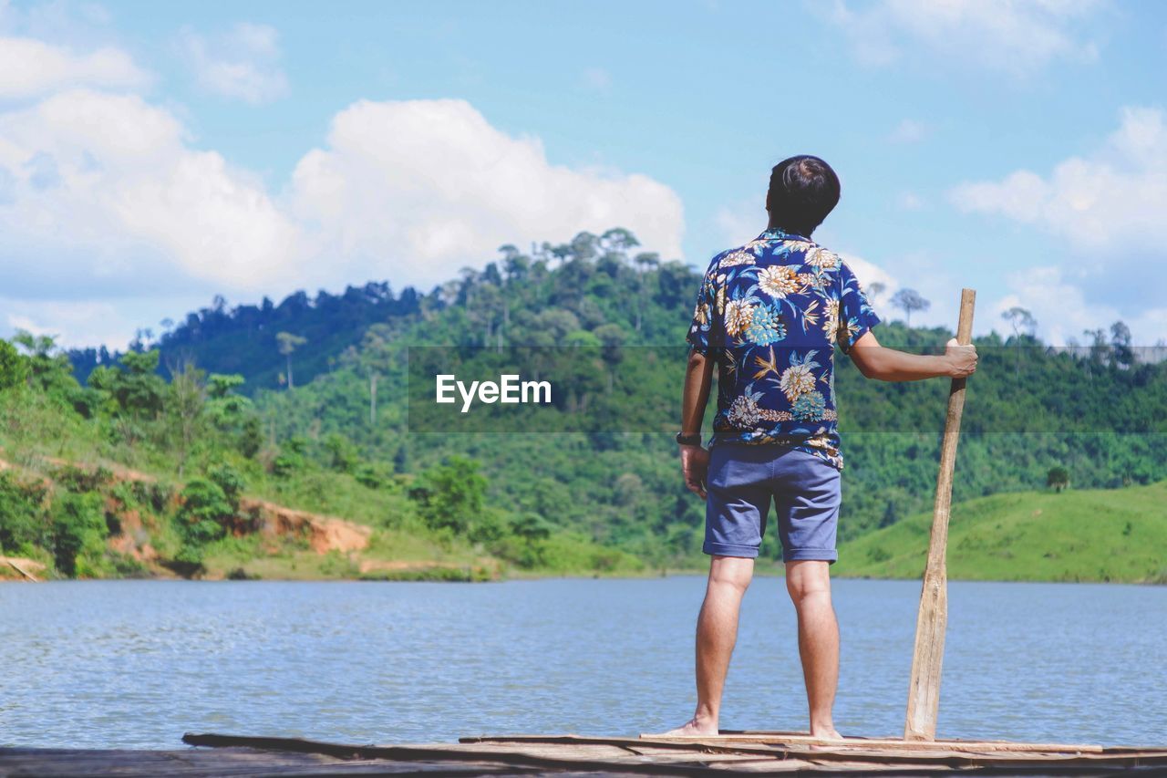 REAR VIEW OF MAN STANDING AGAINST LAKE