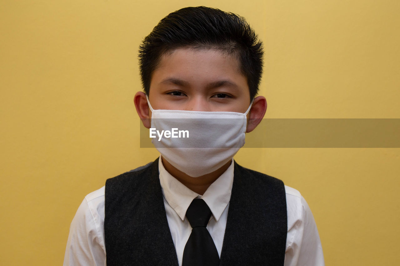 Portrait of boy wearing mask standing against yellow wall