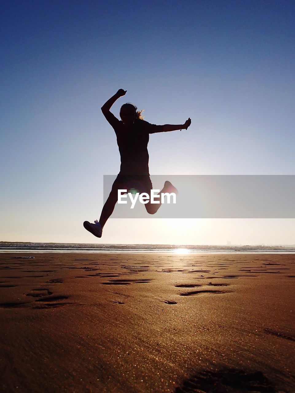 Low angle view of person jumping over beach against clear sky on sunny day
