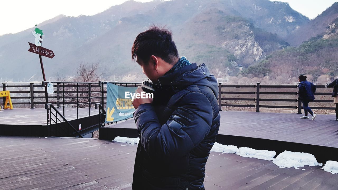 Man drinking while standing against mountain during winter