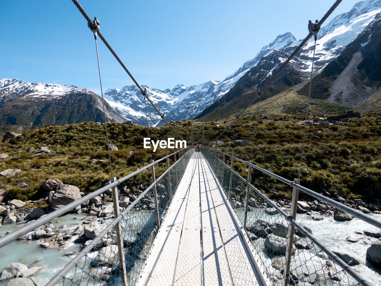 Footbridge over river against snowcapped mountains 