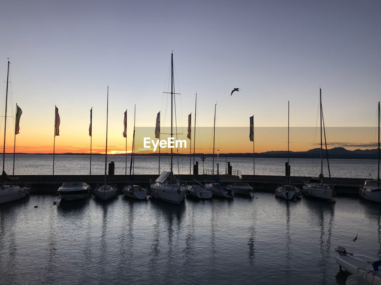 Sailboats moored in sea at sunset