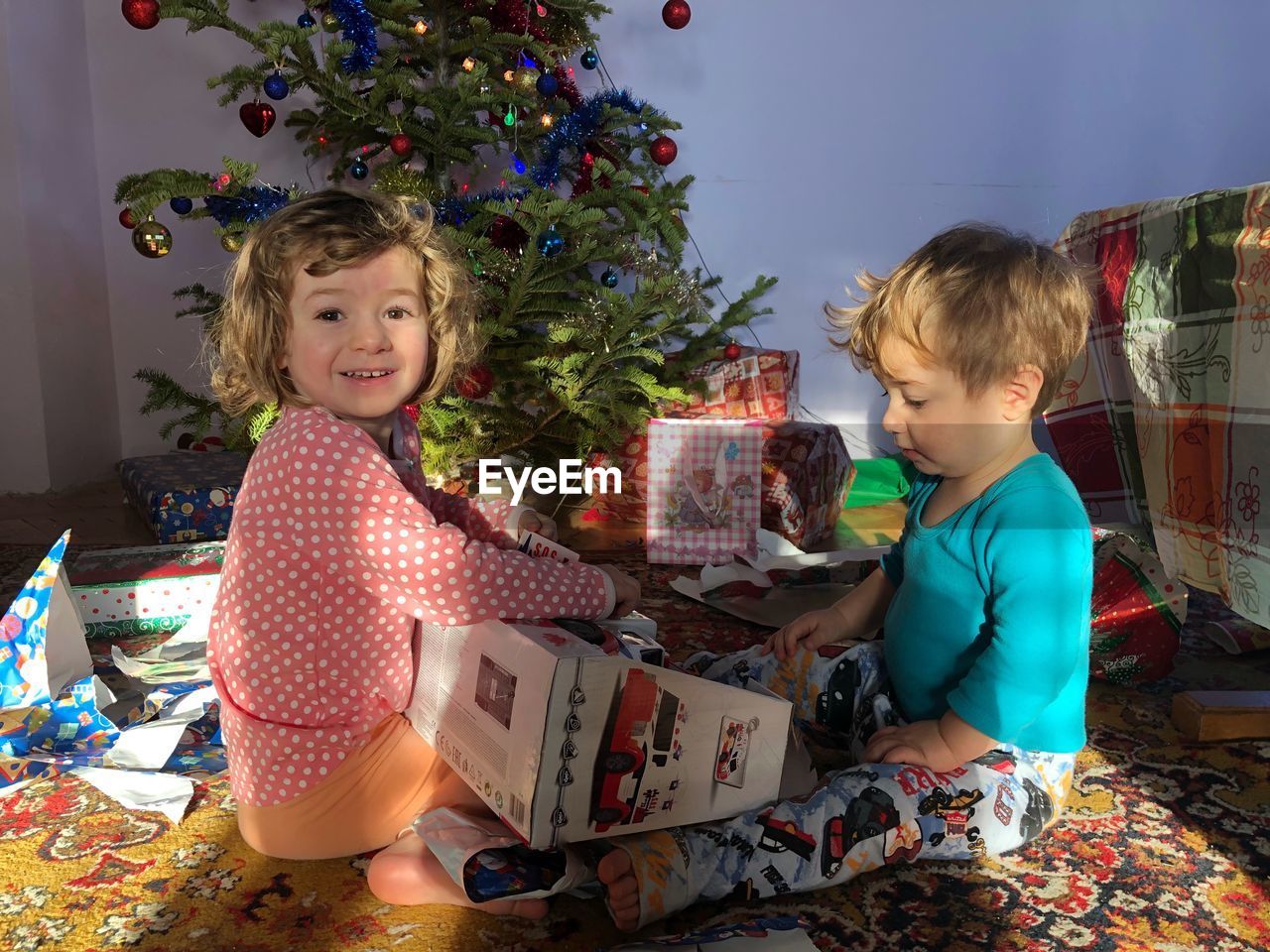 Sisters sitting on bed by christmas tree at home