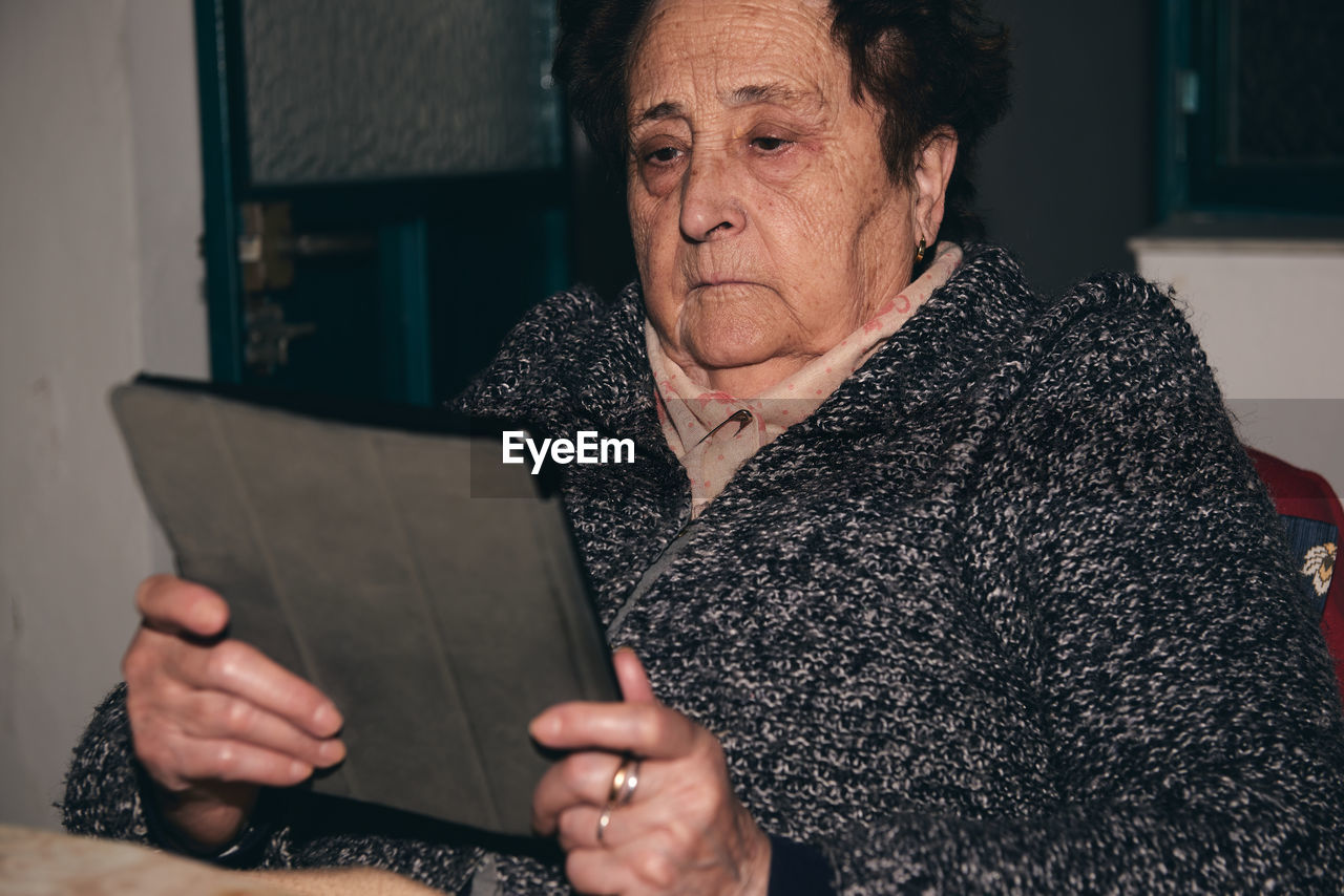 An elderly and surprised woman holding a tablet in her wrinkled hands.