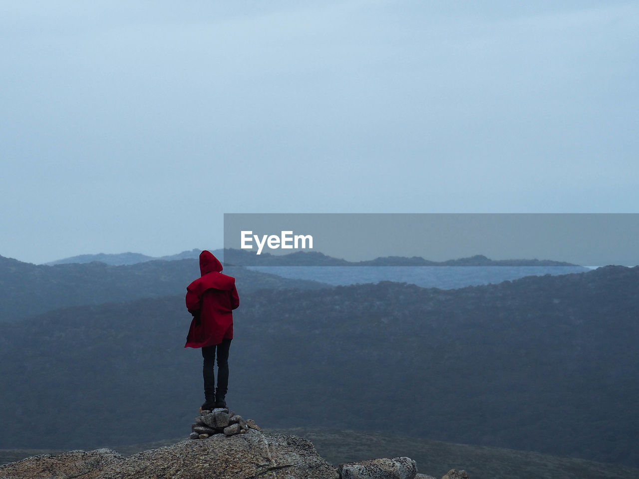 Man standing on cliff in front of mountains against clear sky