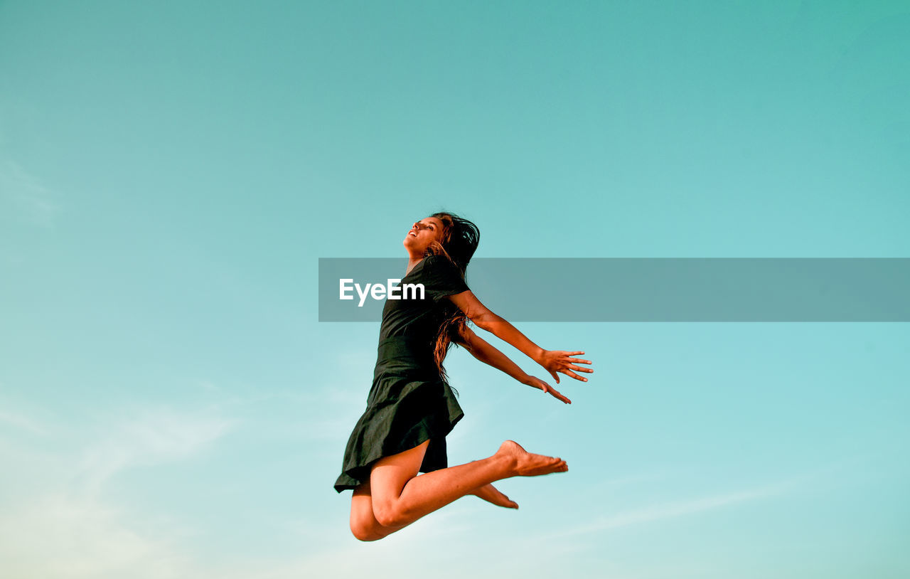 Low angle view of woman jumping against clear blue sky