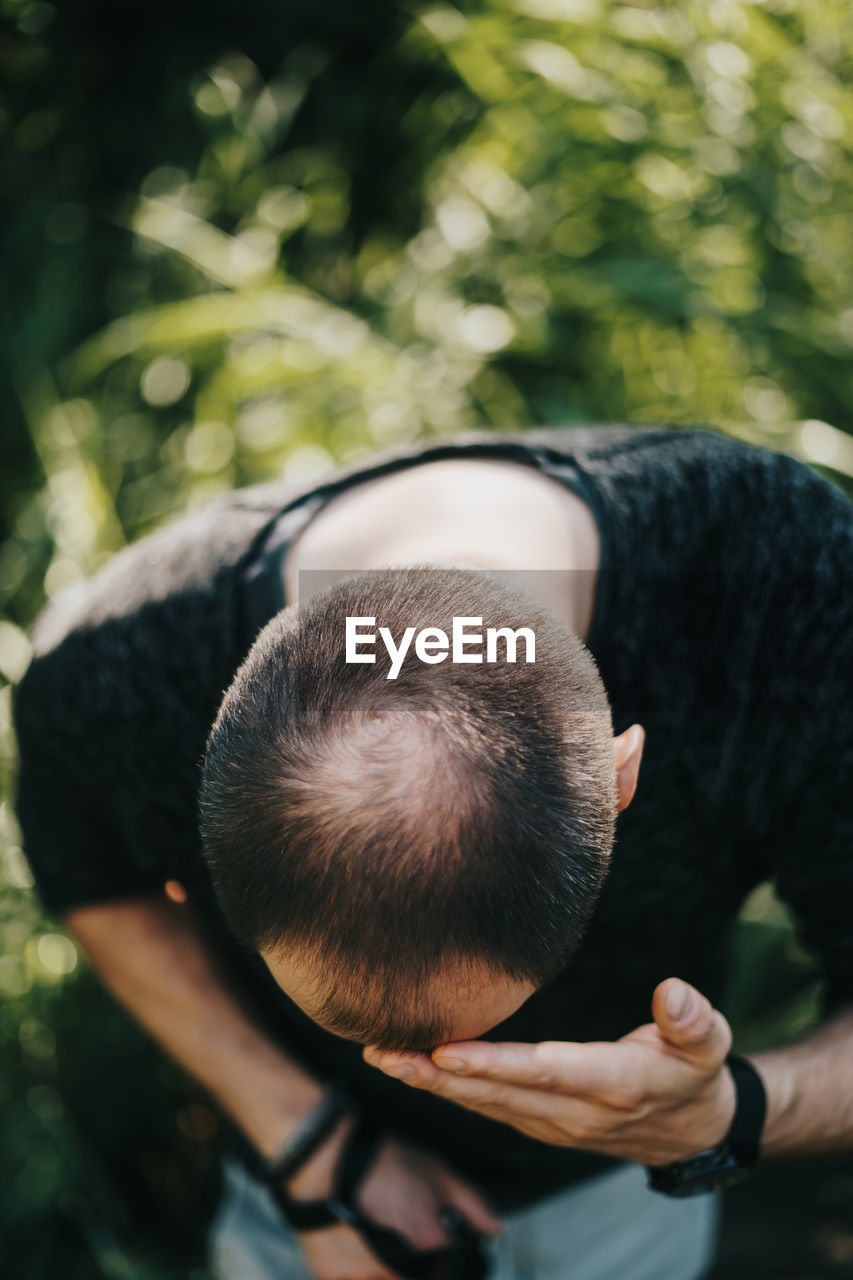 Man touching forehead while standing by plants