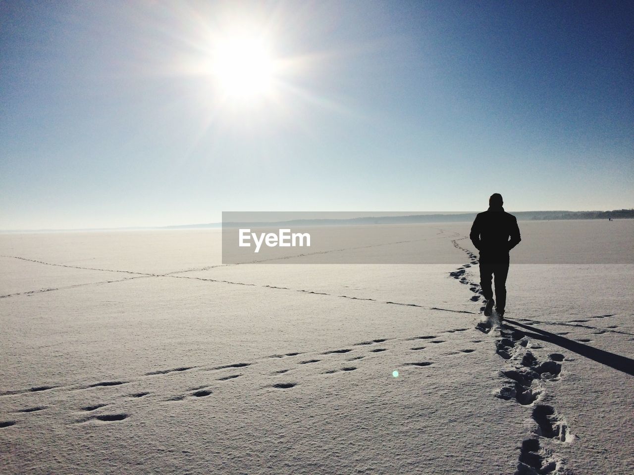 Rear view of man walking on snow covered field against sky