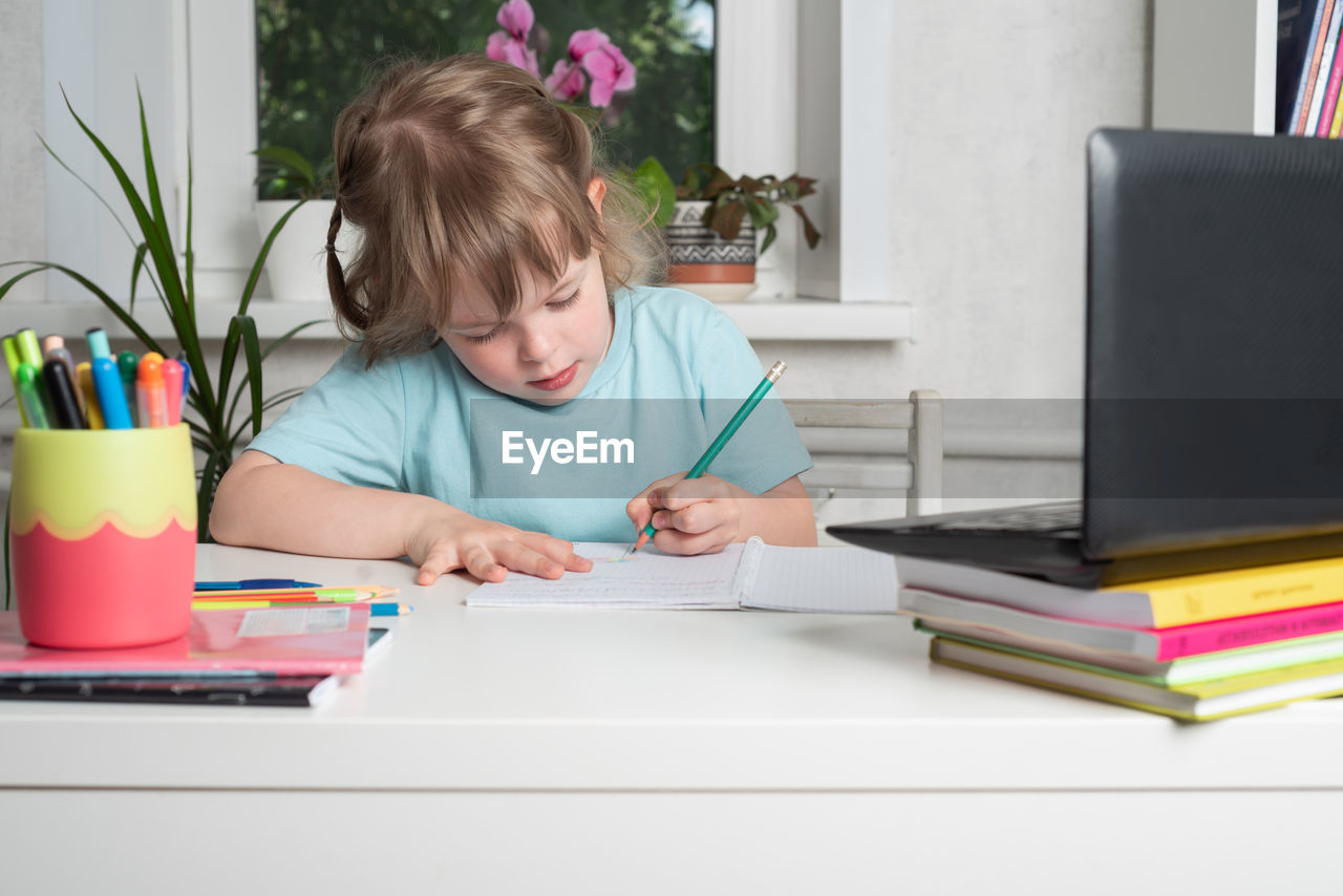 Girl sits at a table with books and a notebook and does her homework. children learning at home.